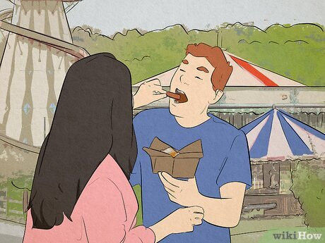 A woman feeding a man. In the background are rides and circus tents.
